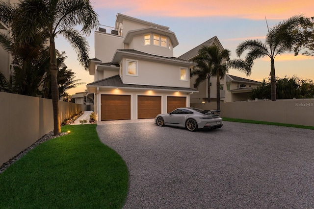 view of front facade featuring driveway, a standing seam roof, fence, an attached garage, and metal roof