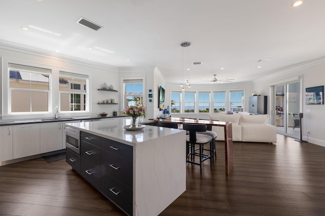 kitchen with visible vents, stainless steel microwave, a kitchen island, crown molding, and dark wood-type flooring