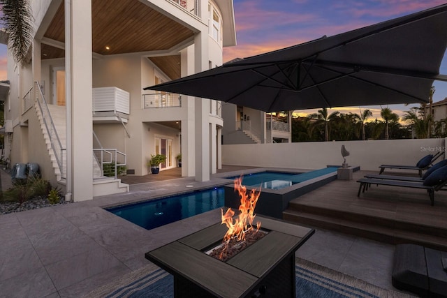 pool at dusk featuring a patio area, a fenced in pool, an outdoor fire pit, and stairs