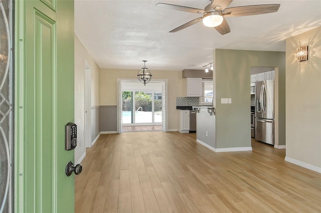 interior space featuring a ceiling fan, light wood-type flooring, a wainscoted wall, and a textured ceiling