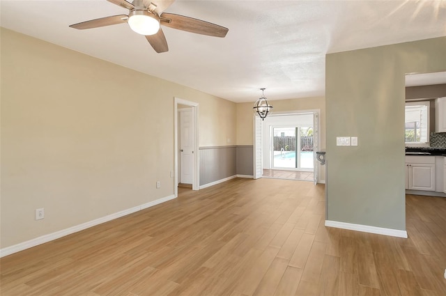 spare room featuring light wood-type flooring, baseboards, and ceiling fan with notable chandelier