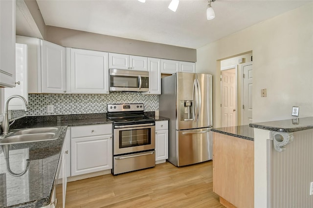 kitchen featuring light wood-style flooring, stainless steel appliances, a sink, white cabinets, and decorative backsplash