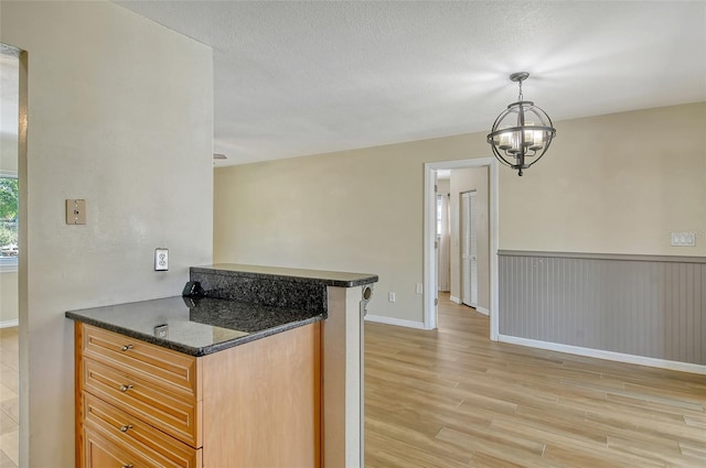 kitchen with a chandelier, a wainscoted wall, a textured ceiling, and light wood finished floors