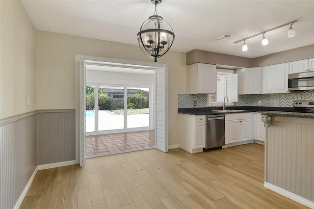 kitchen with a wainscoted wall, a sink, appliances with stainless steel finishes, light wood finished floors, and dark countertops