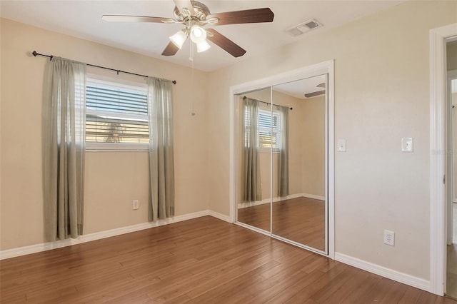 unfurnished bedroom featuring baseboards, visible vents, ceiling fan, wood finished floors, and a closet