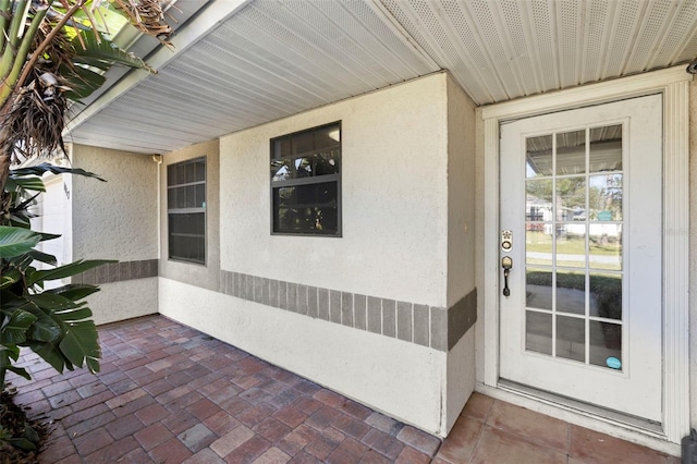 view of exterior entry with stucco siding and a patio area