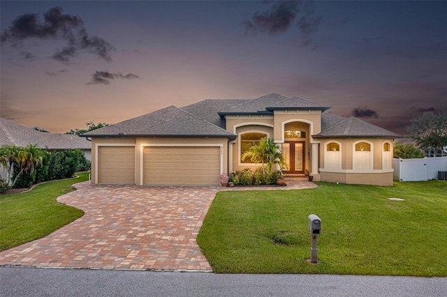 mediterranean / spanish home featuring a garage, stucco siding, fence, decorative driveway, and a front yard