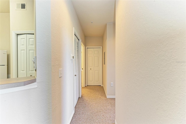 corridor with a textured wall, carpet floors, visible vents, and baseboards