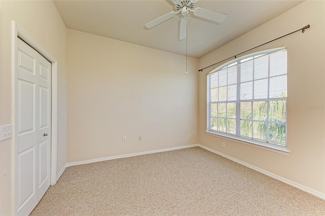 carpeted empty room with a ceiling fan and baseboards