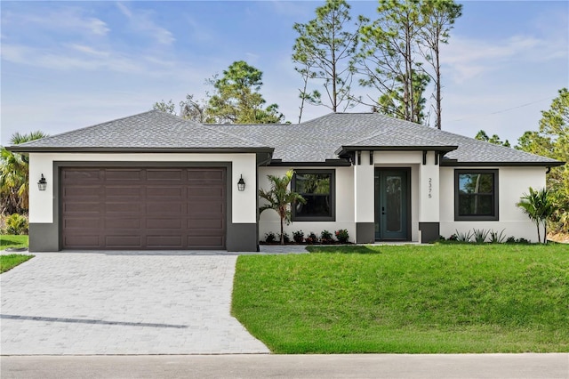 prairie-style house with a front yard, a shingled roof, stucco siding, a garage, and decorative driveway