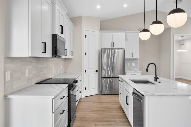 kitchen featuring an island with sink, vaulted ceiling, appliances with stainless steel finishes, light wood-style floors, and a sink