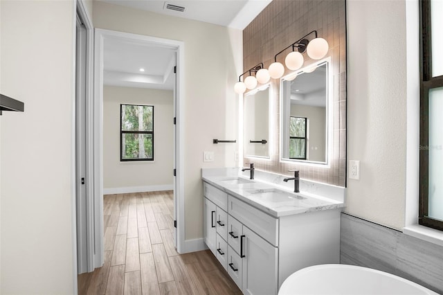 bathroom featuring a sink, a soaking tub, wood finished floors, and double vanity