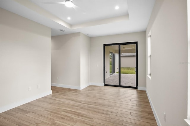 unfurnished room with baseboards, light wood-style floors, and a tray ceiling