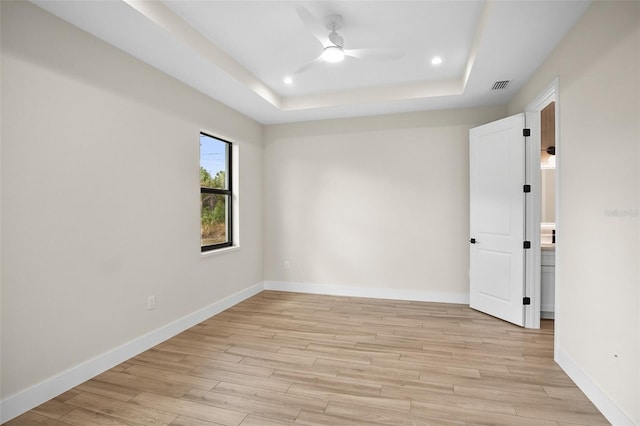 unfurnished room with light wood-type flooring, a tray ceiling, baseboards, and visible vents