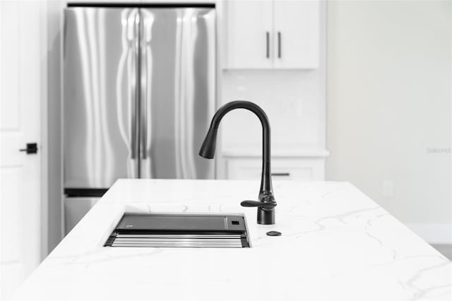 interior details with light stone countertops, white cabinets, and freestanding refrigerator