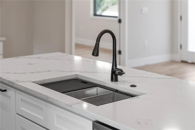 room details with white cabinetry, light stone counters, baseboards, and a sink