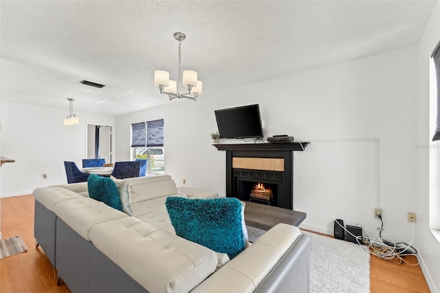 living room with visible vents, a tile fireplace, an inviting chandelier, a textured ceiling, and light wood-type flooring