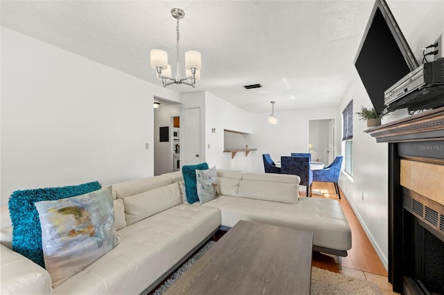 living room featuring a textured ceiling, wood finished floors, baseboards, a tiled fireplace, and an inviting chandelier