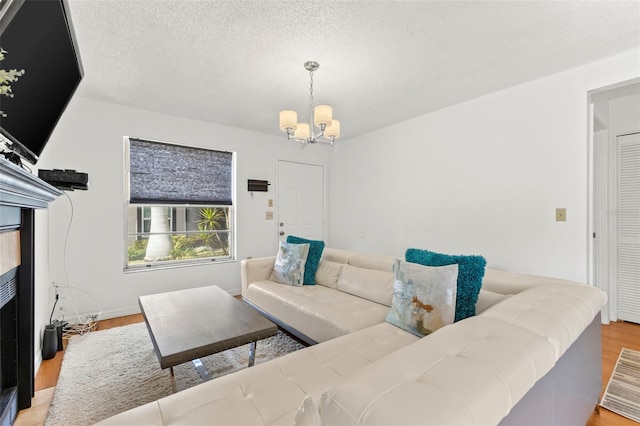 living area with a textured ceiling, light wood finished floors, a fireplace, and a notable chandelier