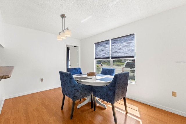 dining area with a textured ceiling, baseboards, and light wood-style floors