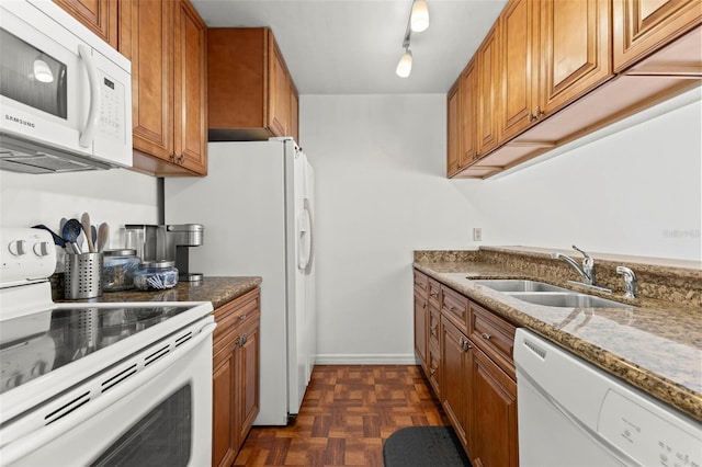 kitchen featuring white appliances, dark stone countertops, a sink, and brown cabinets