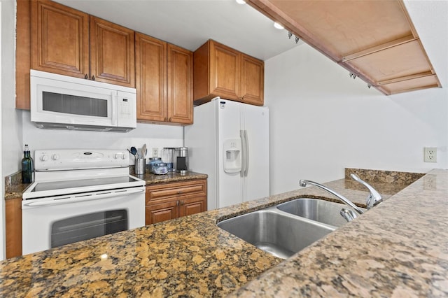 kitchen featuring white appliances, dark stone countertops, brown cabinets, and a sink