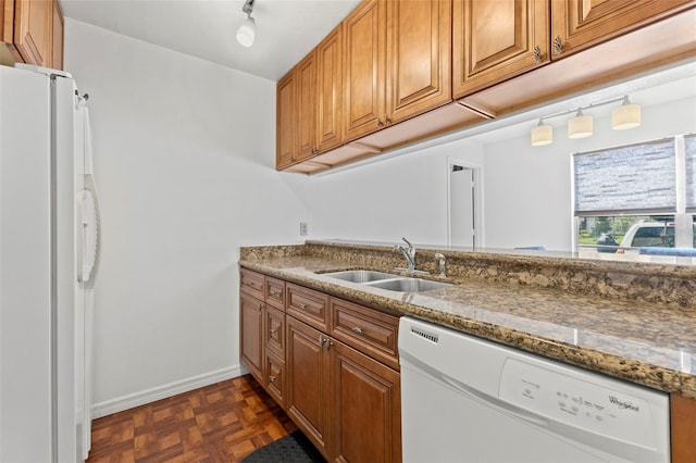 kitchen featuring white appliances, stone counters, brown cabinetry, and a sink