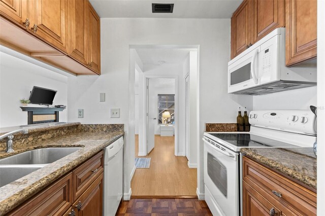 kitchen with visible vents, brown cabinetry, a sink, dark stone countertops, and white appliances