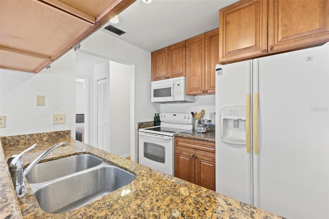 kitchen with white appliances, visible vents, brown cabinetry, dark stone countertops, and a sink