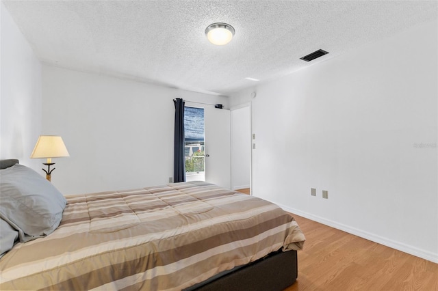 bedroom with visible vents, a textured ceiling, baseboards, and wood finished floors