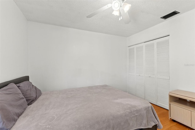 bedroom with a closet, visible vents, light wood-style floors, a ceiling fan, and a textured ceiling