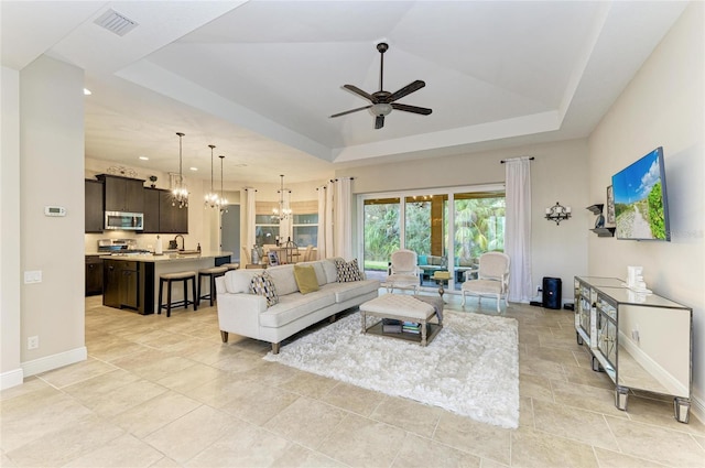 living room featuring a tray ceiling, recessed lighting, visible vents, baseboards, and ceiling fan with notable chandelier