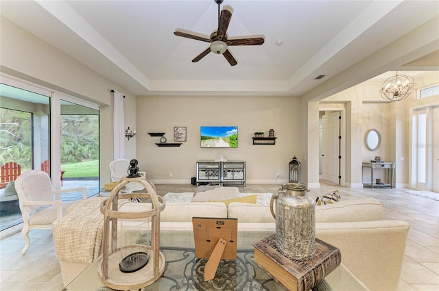 living room with light tile patterned floors, baseboards, a raised ceiling, and ceiling fan with notable chandelier