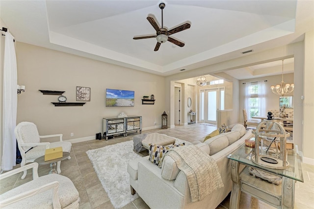 tiled living area featuring baseboards, visible vents, a tray ceiling, and ceiling fan with notable chandelier