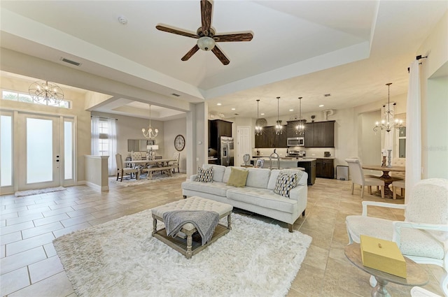 living room featuring light tile patterned floors, recessed lighting, a raised ceiling, baseboards, and ceiling fan with notable chandelier