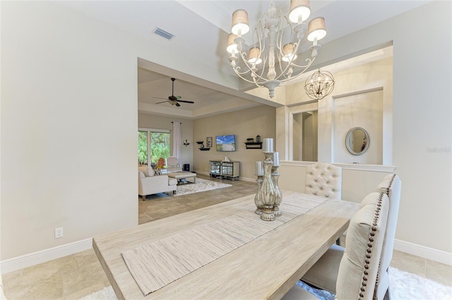 tiled dining space featuring baseboards, visible vents, a tray ceiling, and ceiling fan with notable chandelier