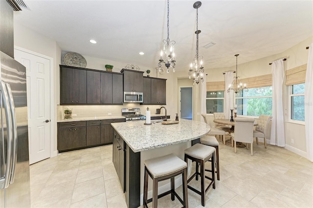 kitchen featuring pendant lighting, appliances with stainless steel finishes, a kitchen island with sink, dark brown cabinets, and a kitchen breakfast bar