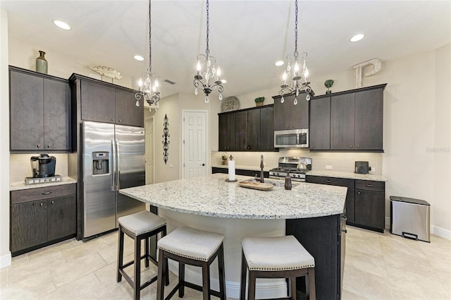 kitchen featuring hanging light fixtures, appliances with stainless steel finishes, decorative backsplash, an island with sink, and a kitchen bar