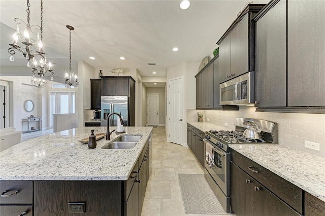 kitchen with light stone counters, a kitchen island with sink, stainless steel appliances, a sink, and decorative backsplash