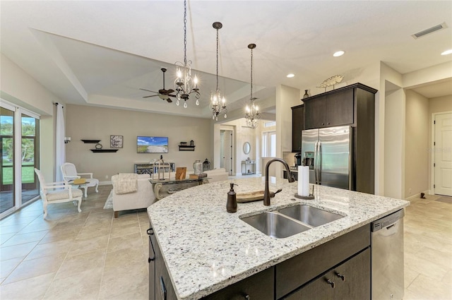 kitchen featuring stainless steel appliances, a sink, dark brown cabinets, a tray ceiling, and an island with sink