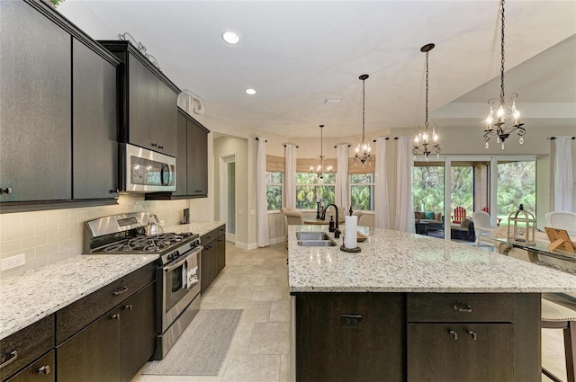 kitchen with tasteful backsplash, an island with sink, appliances with stainless steel finishes, pendant lighting, and a sink