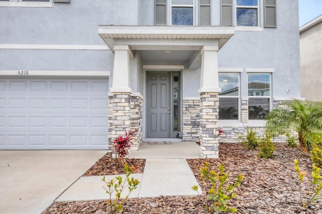 doorway to property featuring stone siding, concrete driveway, and stucco siding