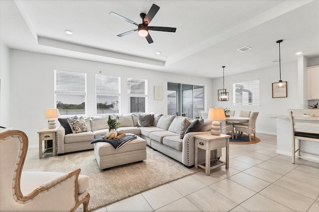 living area featuring a wealth of natural light, a tray ceiling, visible vents, and light tile patterned floors