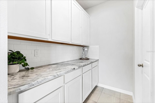 kitchen featuring tasteful backsplash, white cabinetry, light tile patterned flooring, light stone countertops, and baseboards