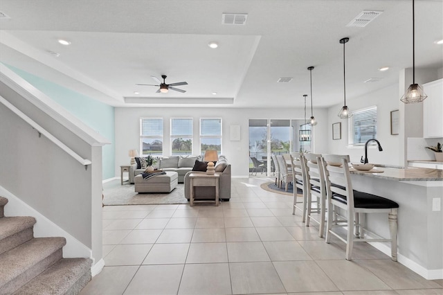 living area featuring light tile patterned floors, stairs, visible vents, and a raised ceiling