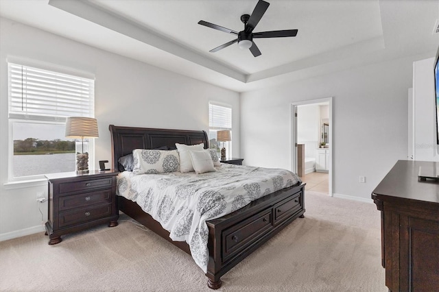 bedroom featuring a tray ceiling, light carpet, connected bathroom, and baseboards