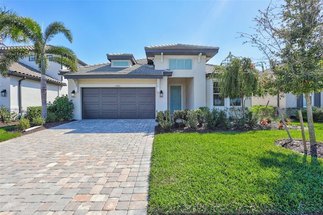 prairie-style house with a garage, a front lawn, decorative driveway, and stucco siding