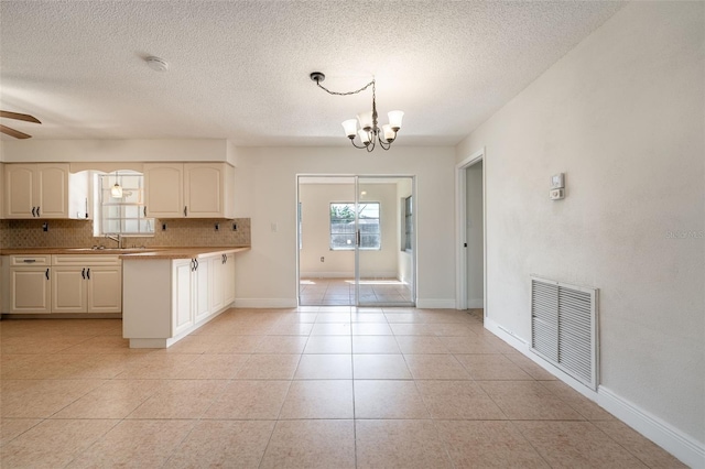 kitchen featuring visible vents, decorative backsplash, light tile patterned flooring, a peninsula, and ceiling fan with notable chandelier