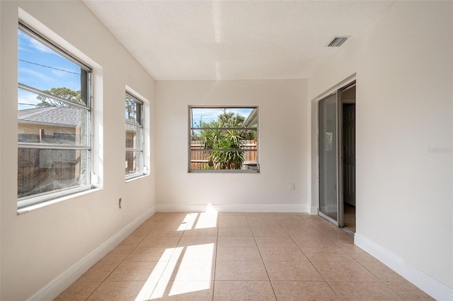 spare room featuring light tile patterned floors, a wealth of natural light, visible vents, and baseboards