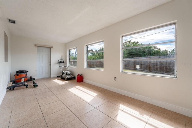 exercise area with tile patterned flooring, visible vents, a textured ceiling, and baseboards